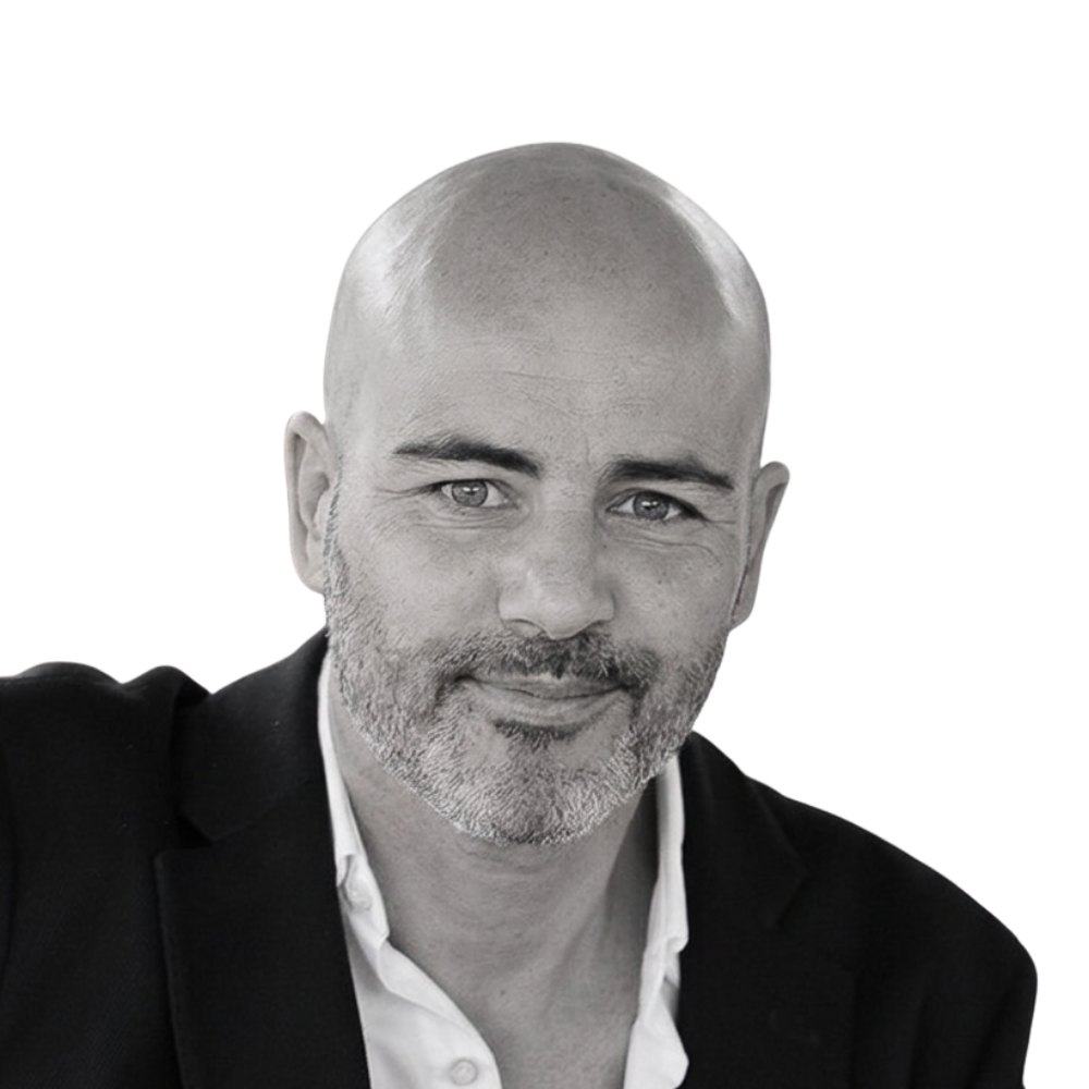 Elad Alon, black-and-white portrait: shaved head, grey beard, dark jacket over a white shirt