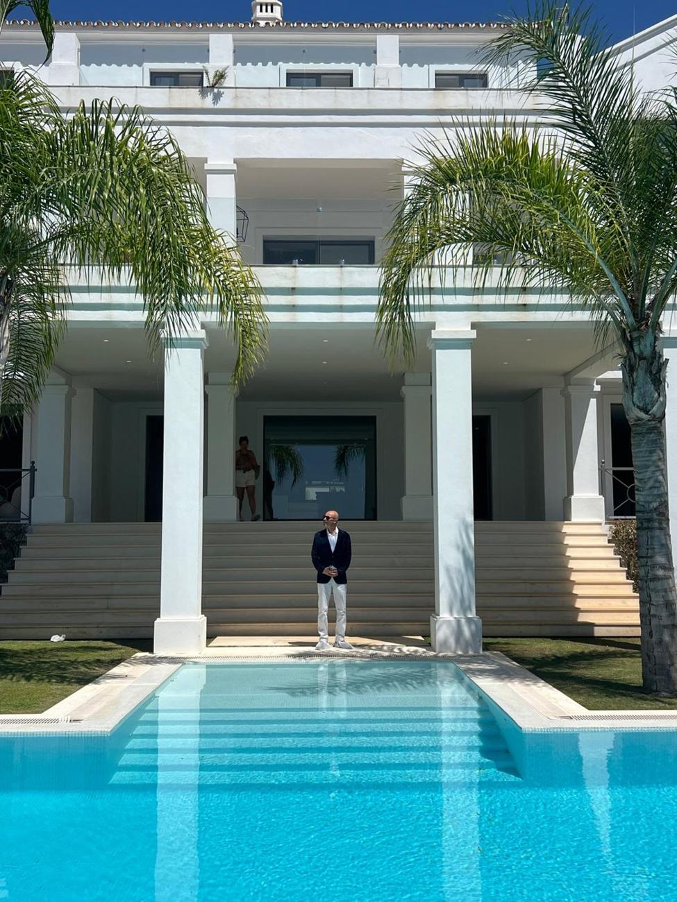 Elad Alon at the top of the steps of a white villa, with a long pool in front