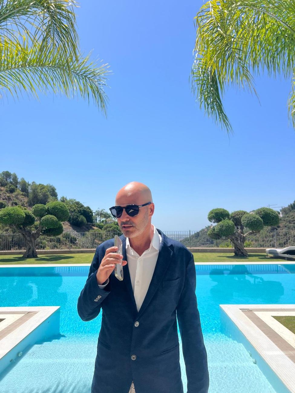 Elad Alon beside a swimming pool with palm trees and hills behind