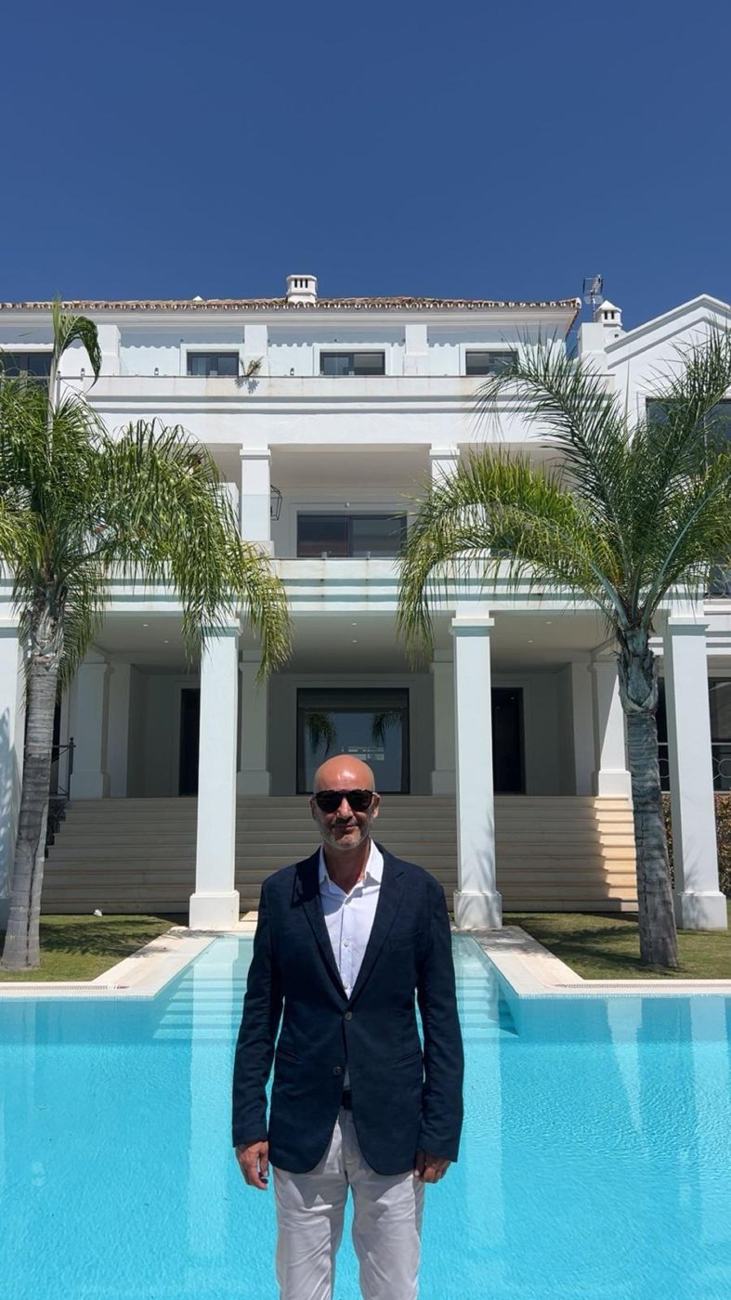 Elad Alon in front of a white villa with columns and palm trees